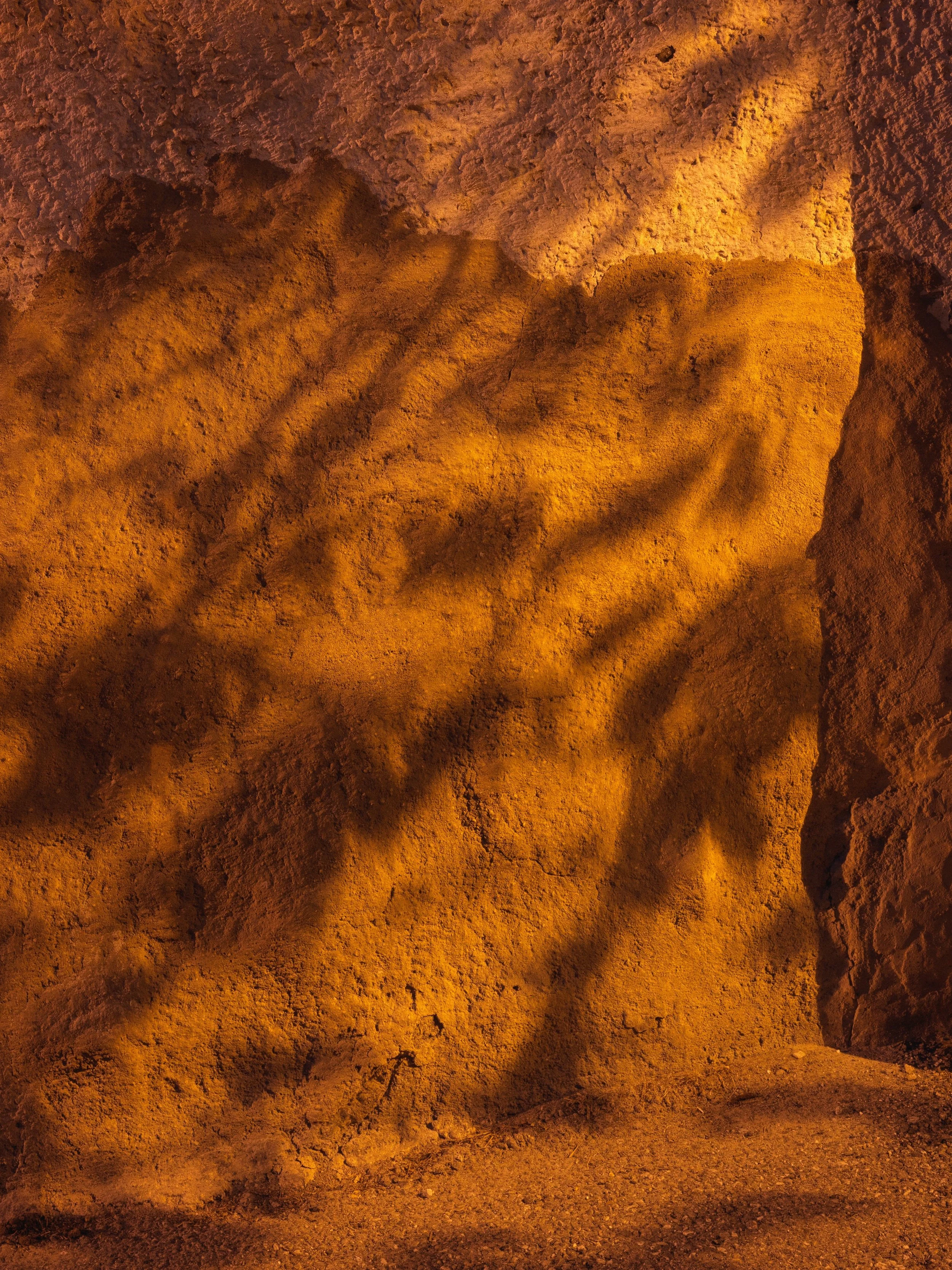 Close-up of orange-colored rock surface with shadows cast on it.