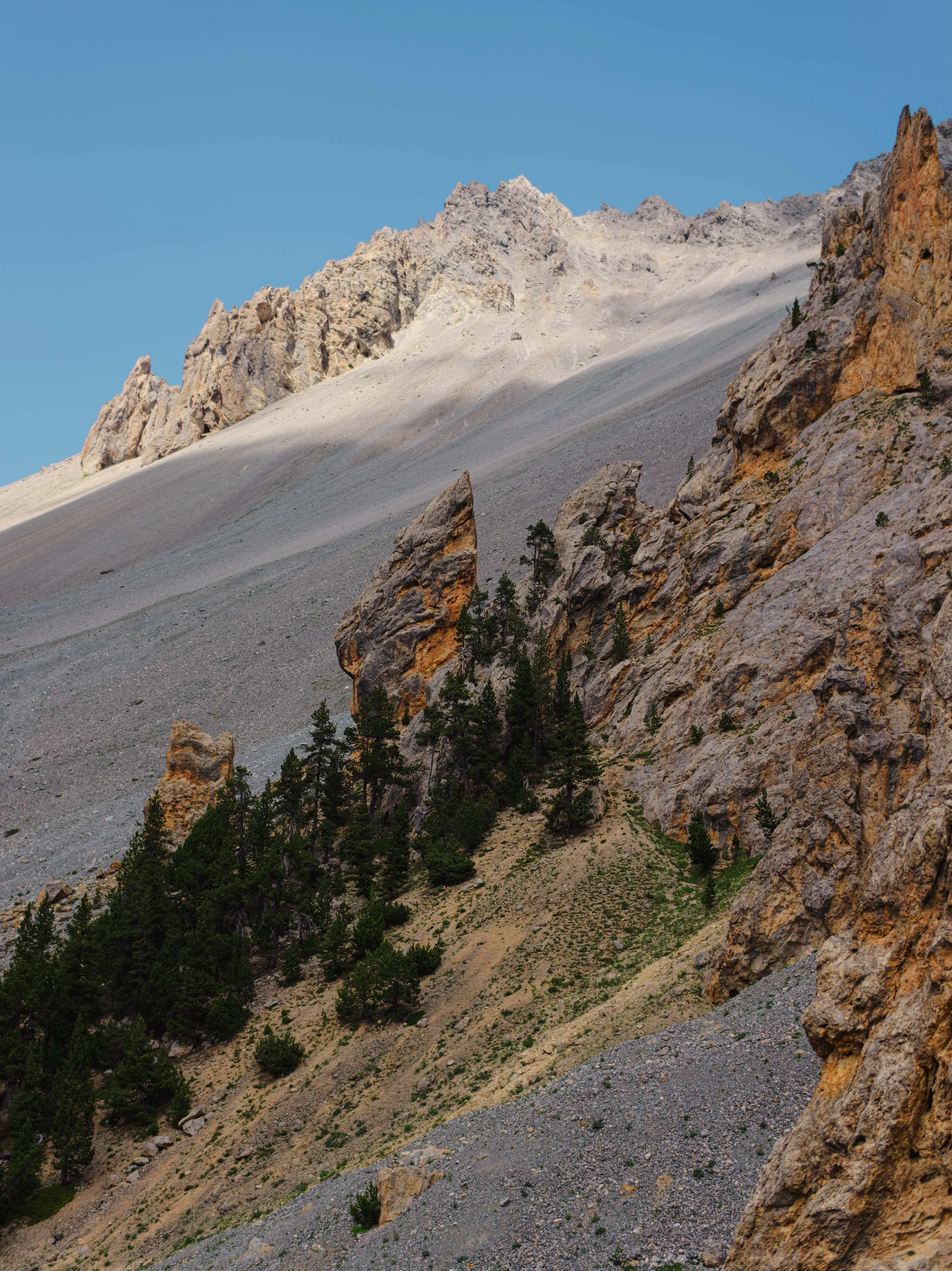 Mountain landscape with rocky slopes, green trees, and blue sky.