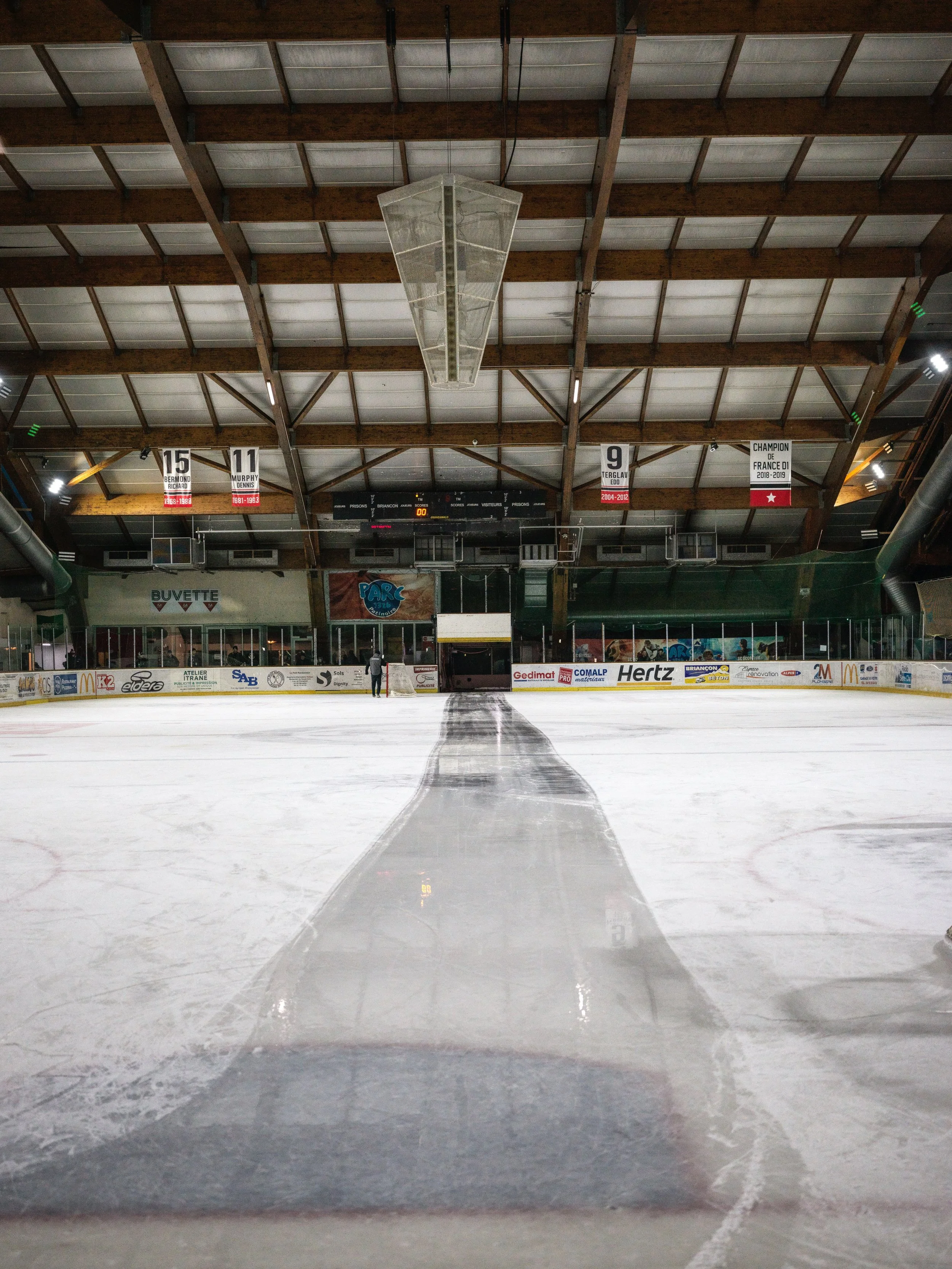 Empty indoor ice hockey rink with a strip of black referees tape on the ice, and banners hanging from the ceiling.