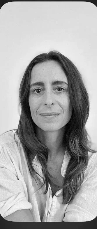 A woman with long brown hair and light skin, wearing a light blue shirt, smiling against a plain white background. EFT Couples Therapist. 