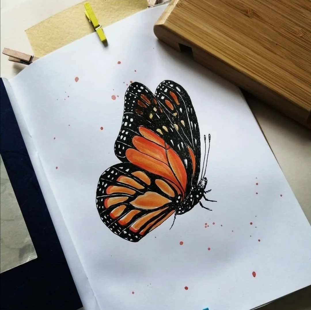 Dessin d'un papillon coloré, avec des ailes orange et noires, posé sur une feuille blanche, avec quelques taches de peinture ou d'encre autour.