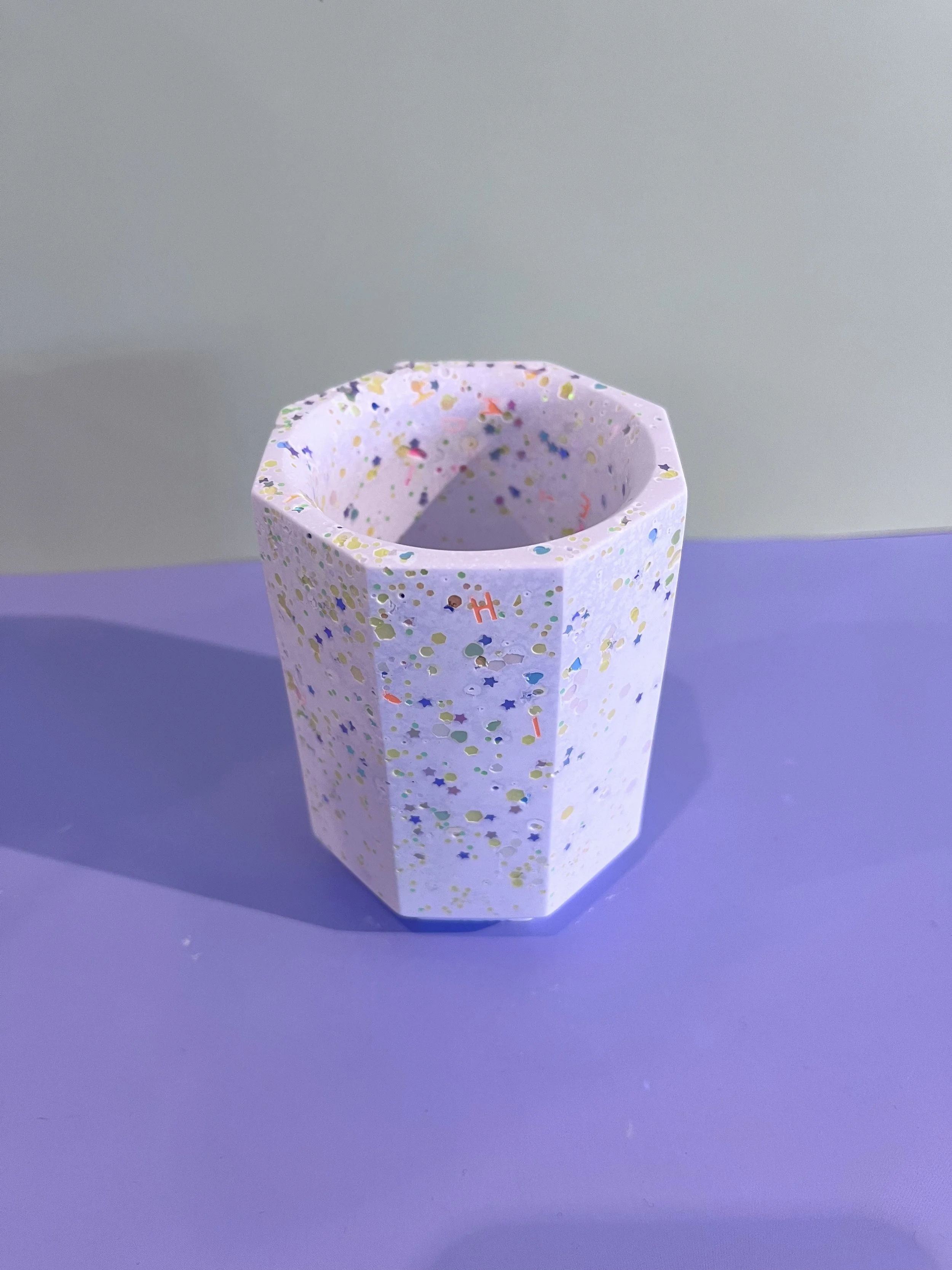Verre en papier décoré avec des confettis multicolores placé sur une surface violette