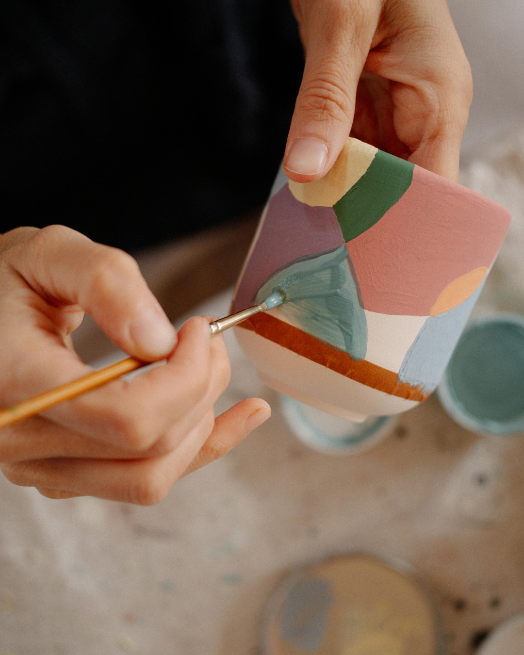 Une personne peint un pot en céramique avec des formes géométriques colorées.