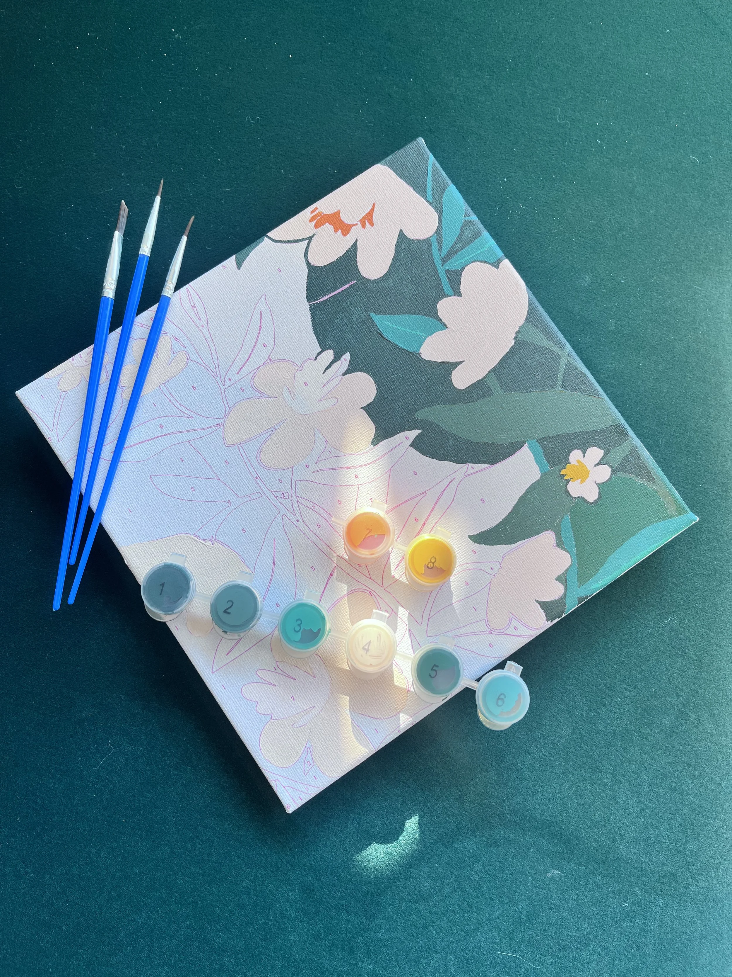 Un tableau de peinture avec des pinceaux bleus et des petits pots de peinture, posé sur une surface foncée