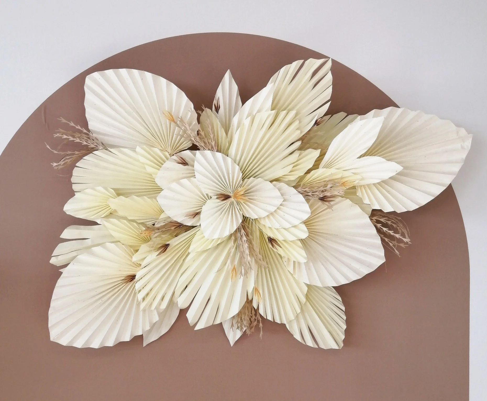Composition artistique de fleurs en papier texturé de couleur crème sur un fond marron.