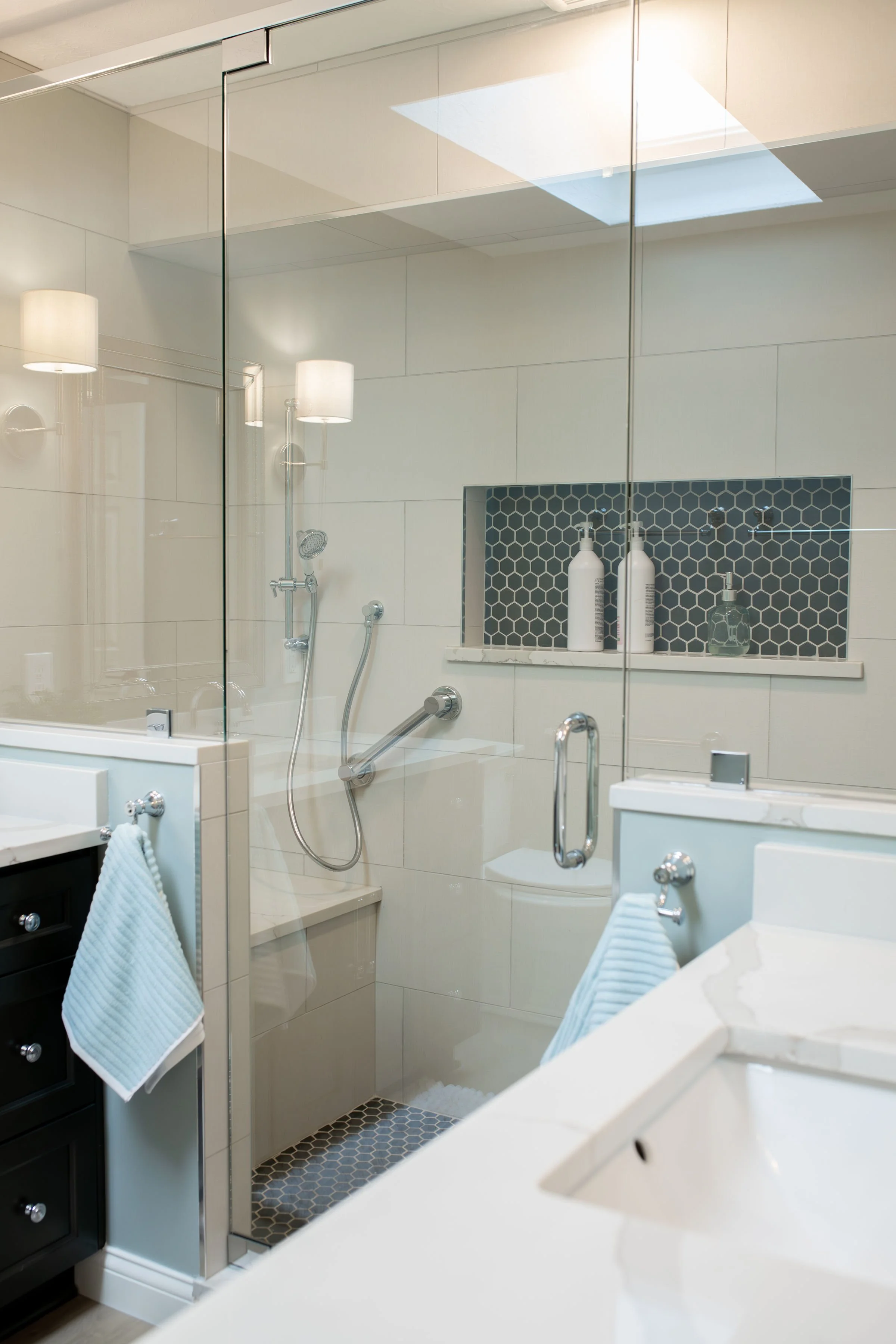Bathroom with glass shower enclosure, black and white decor, and towels hanging on hooks.