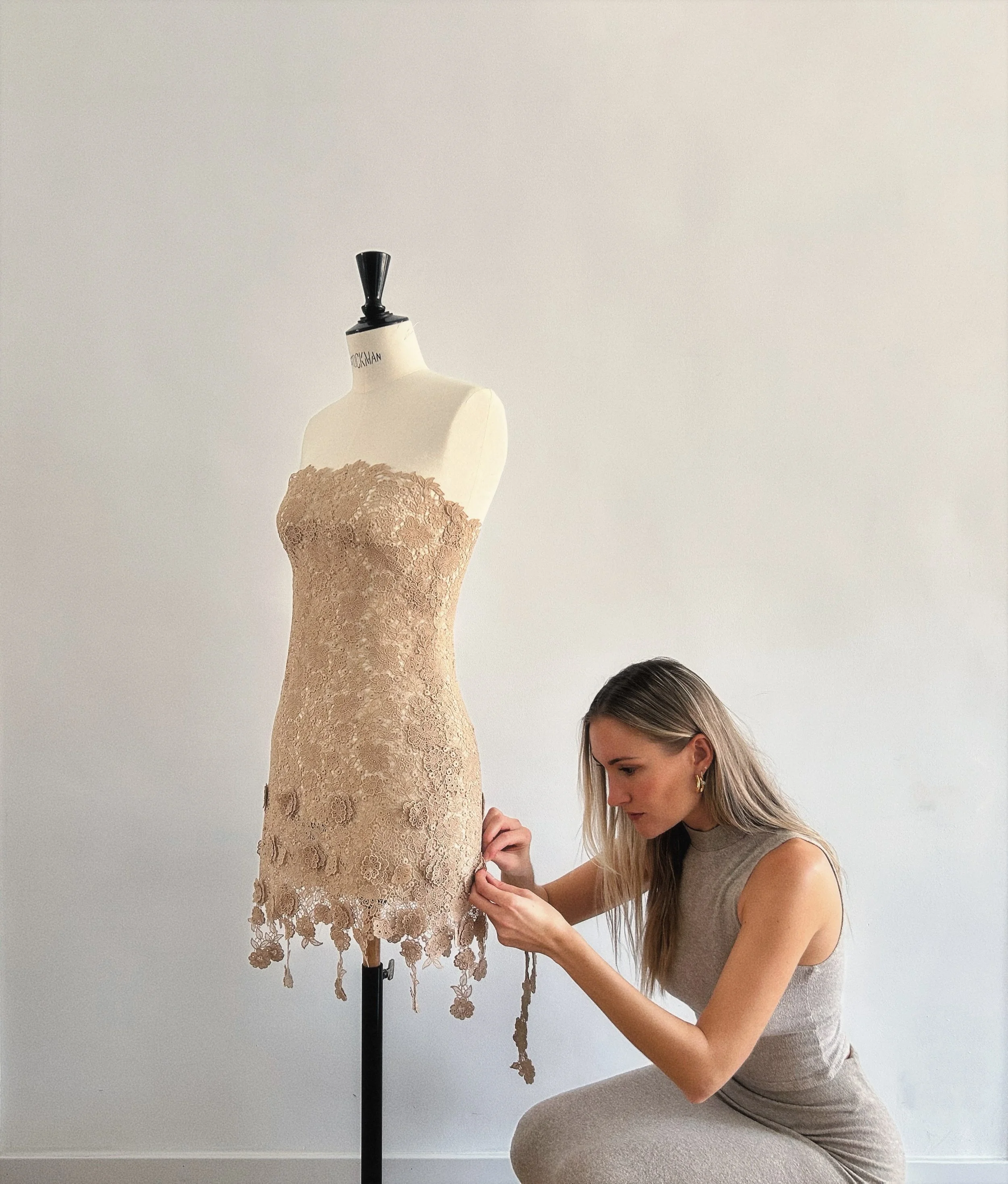 Kassandra Liot adjusting a lace couture dress by hand on a mannequin in her Madrid atelier