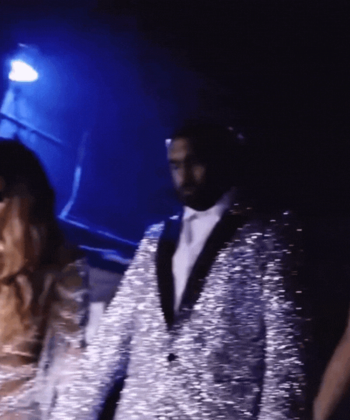 Man wearing a shiny silver blazer at a night event with dark background.