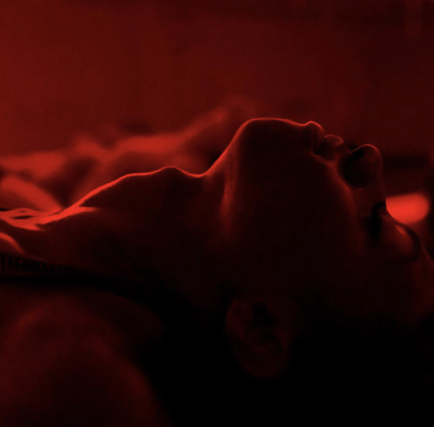 A person lying down with their head tilted back, illuminated by red lighting, creating a dramatic silhouette.