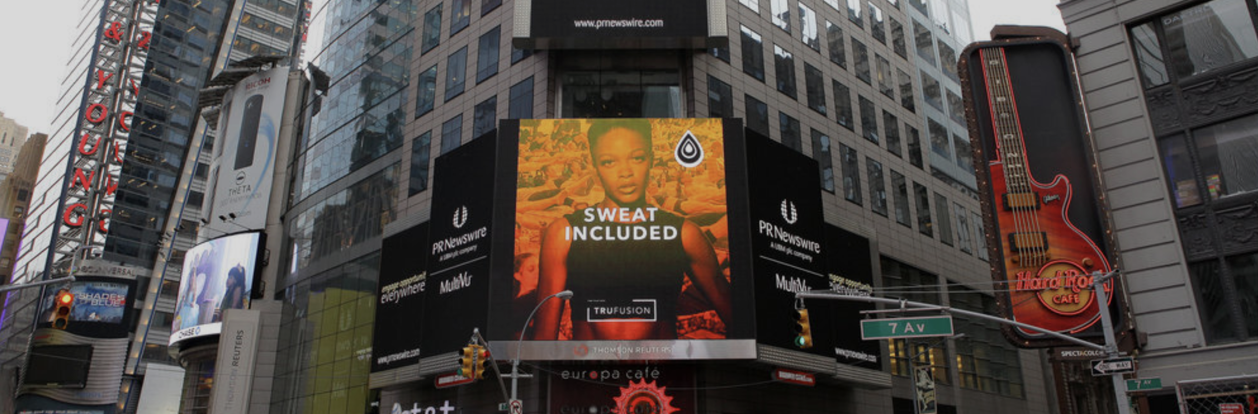 Digital billboard in Times Square showing an advertisement with a girl and the text "Sweat Included".