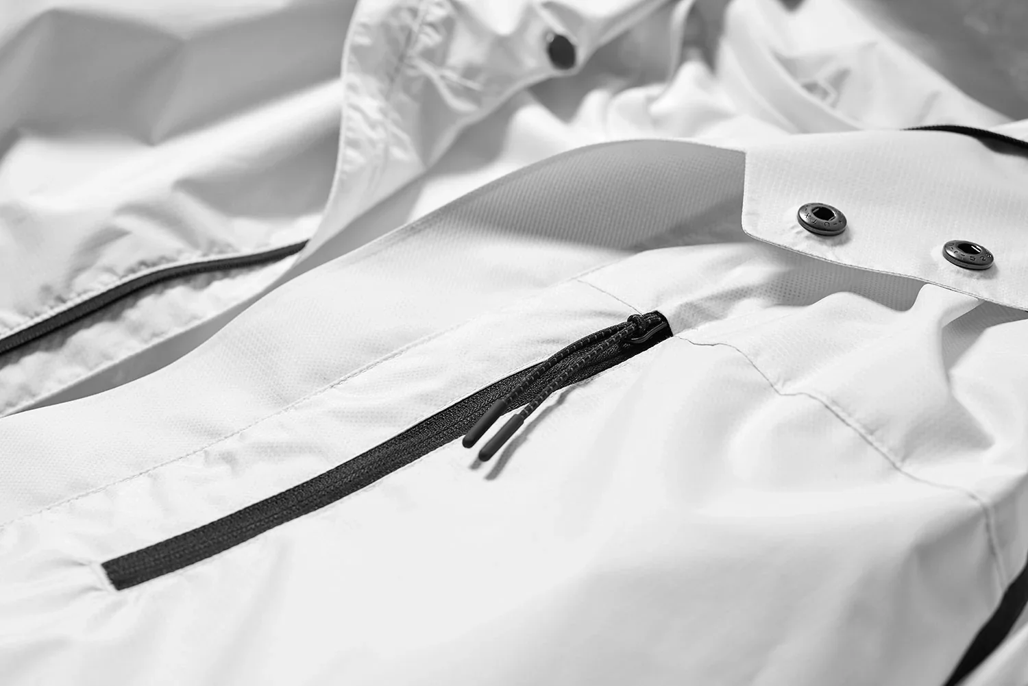 Close-up of a white outdoor jacket with black zipper and snap buttons, lying flat.