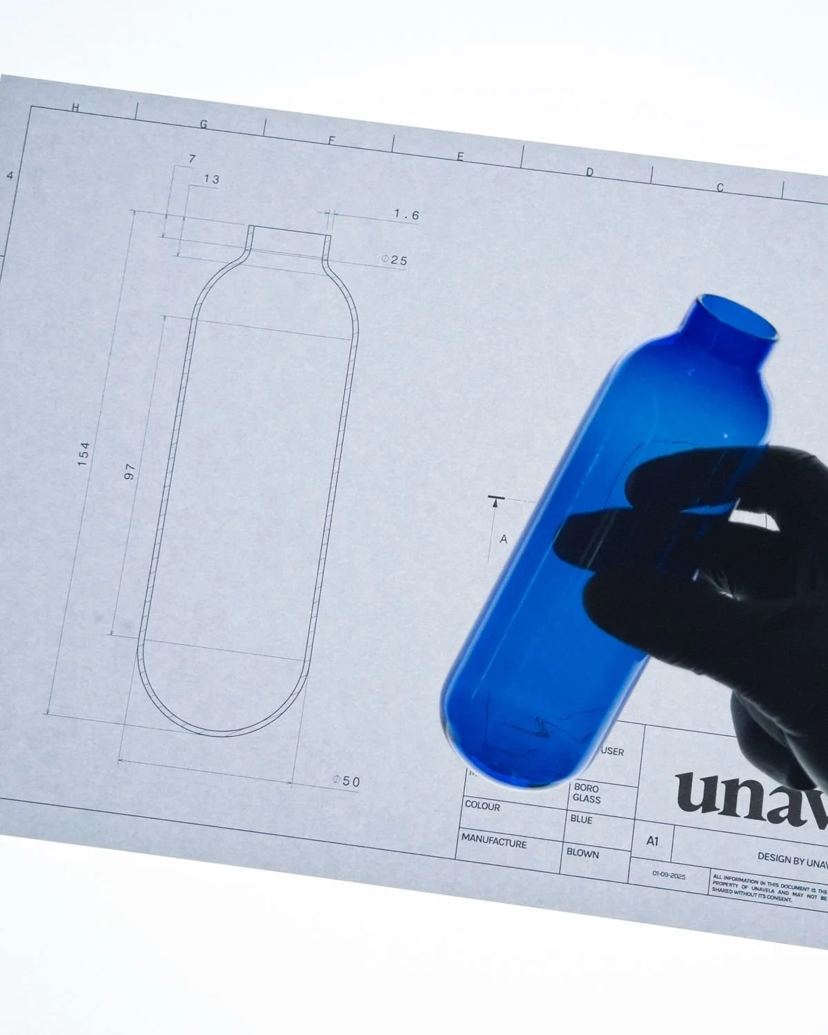 Blueprint drawing of a glass bottle on a white table with a person holding a blue glass bottle in their hand.