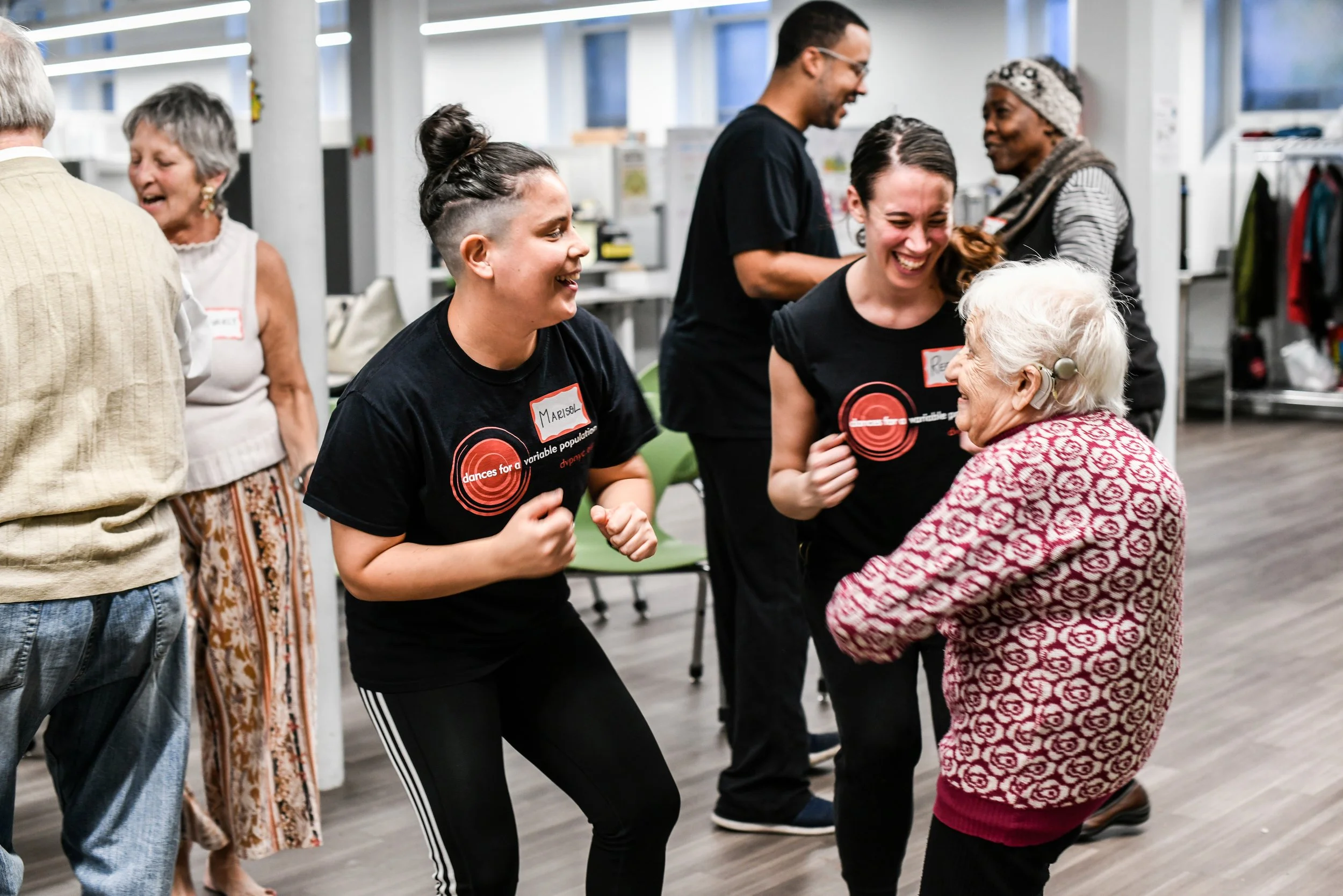 Group of people of various ages dancing and interacting joyfully in a community center.
