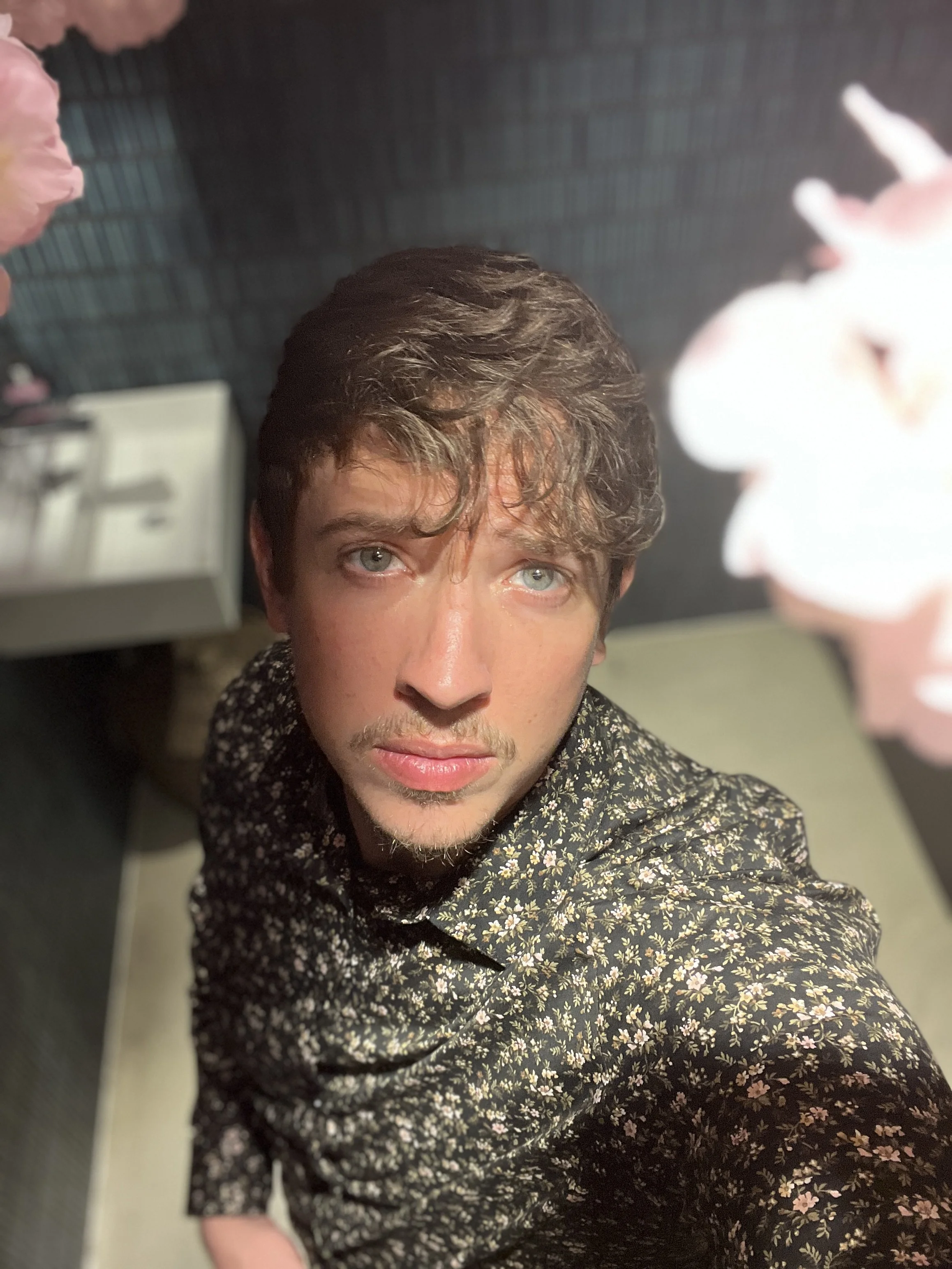 Person taking a selfie in a dimly lit room with floral patterns.