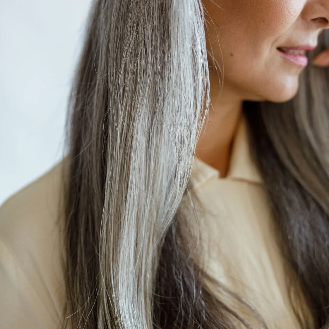 Close-up of a woman with long, straight, grayish-blonde hair, smiling softly and wearing a light-colored top.
