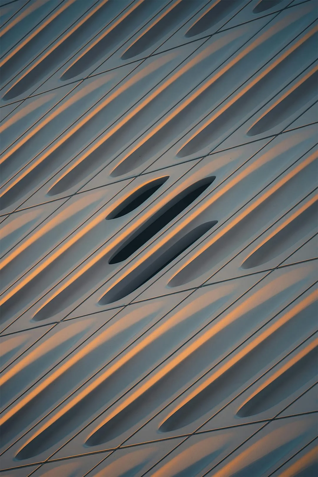 Close-up view of a modern architectural building facade with elongated oval-shaped vents and diagonal lines in a repetitive pattern.