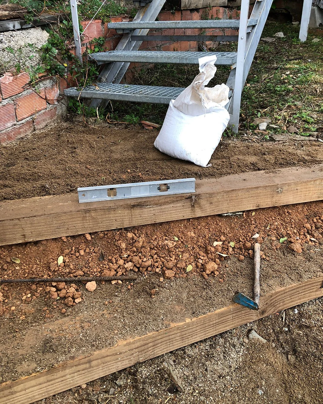 Traviesa de pino sobre terreno arcilloso, nivel y herramientas de jardinería