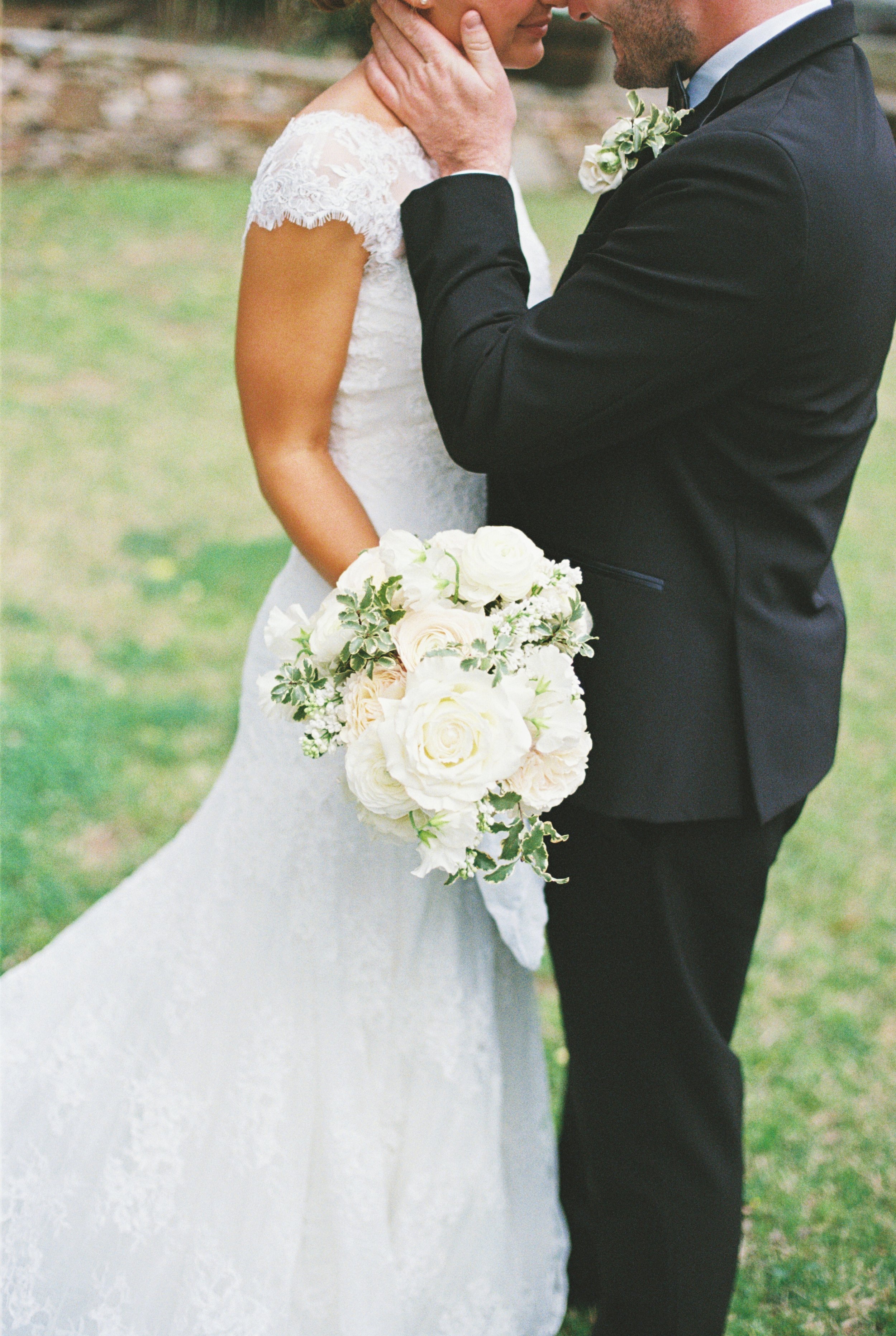 Bride and groom embracing outdoors, bride holding a bouquet of white roses.
