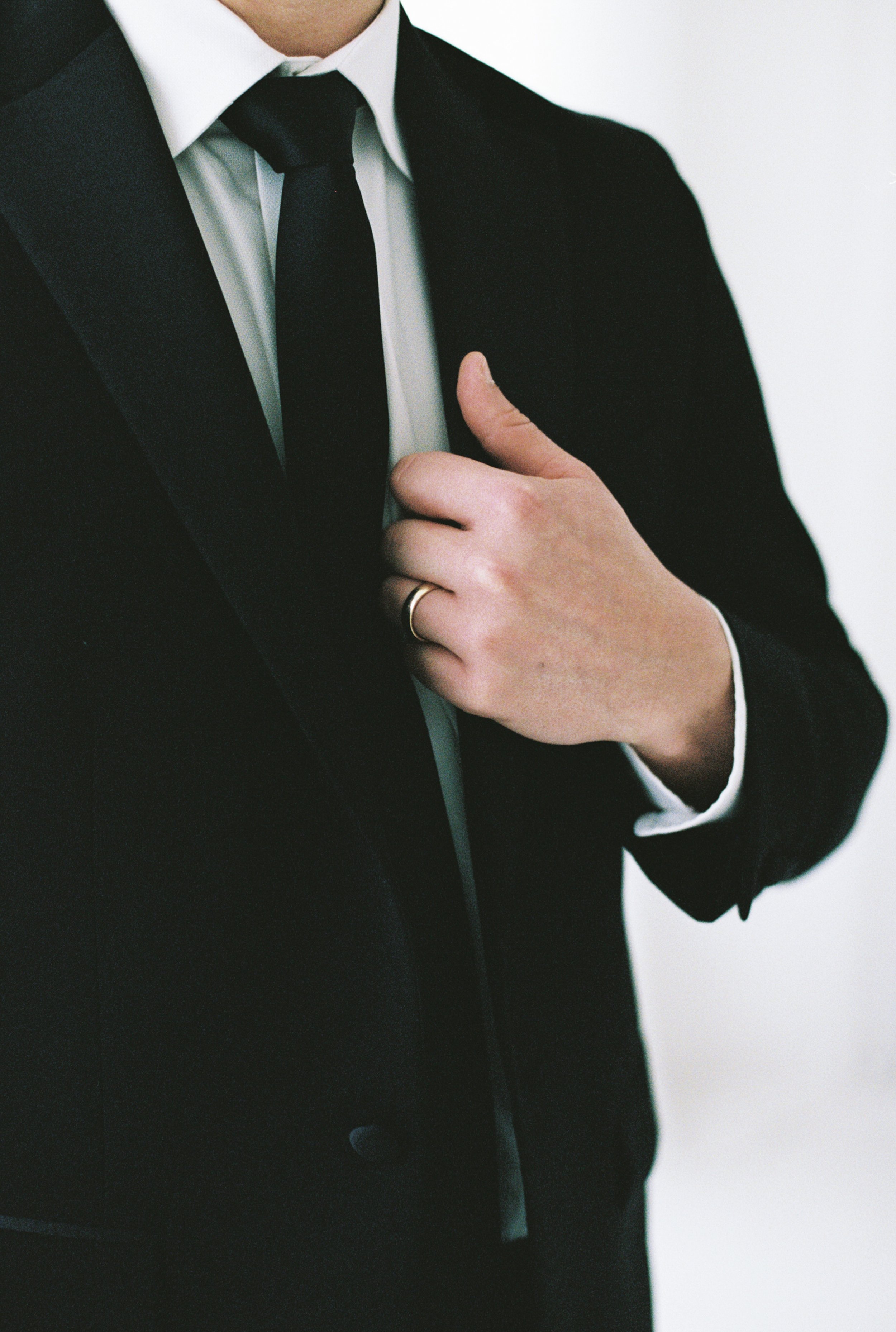 Person adjusting suit and tie, wearing a wedding ring