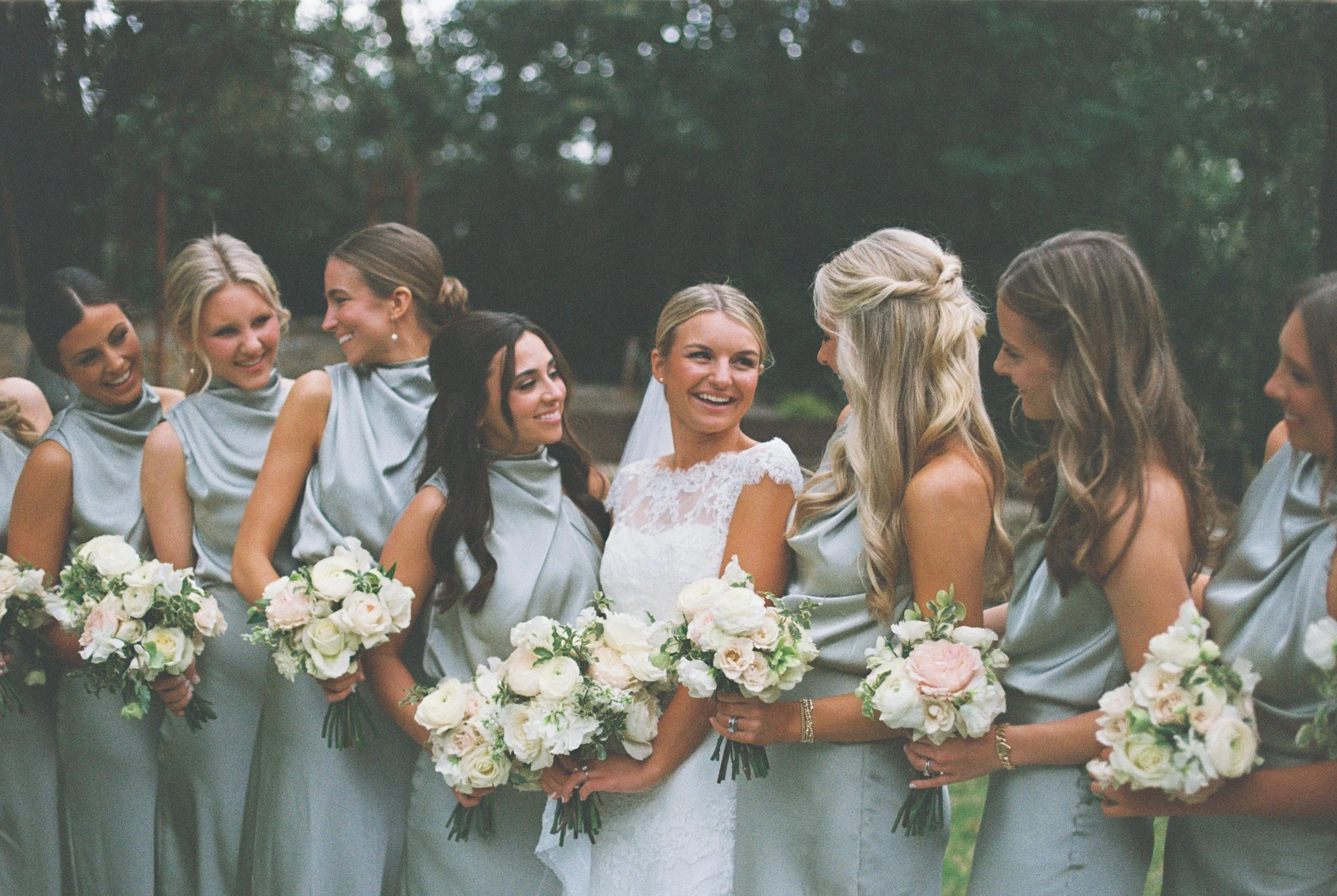 Bride with bridesmaids holding bouquets in outdoor setting.