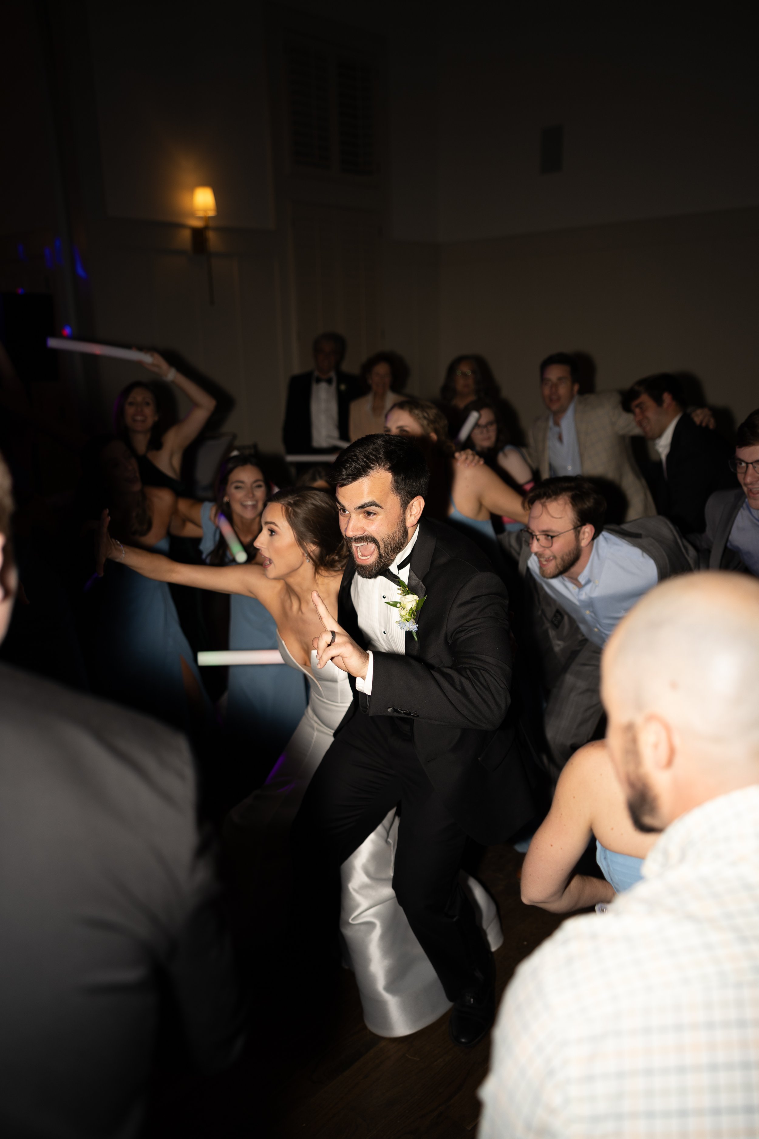 A celebration with people in formal attire, including a groom and a bride, dancing and smiling.