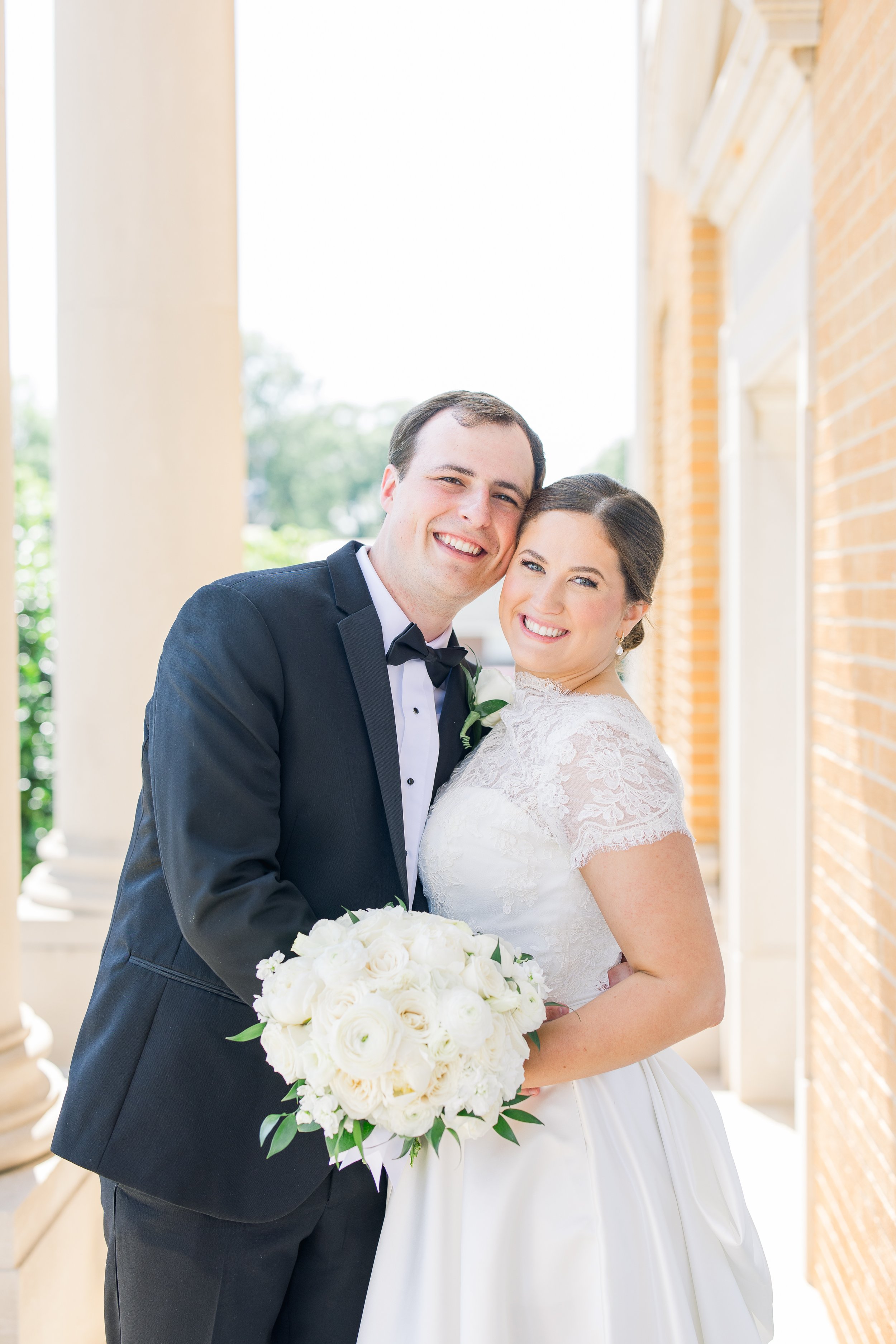 Bride and groom smiling, bride holding a white rose bouquet.