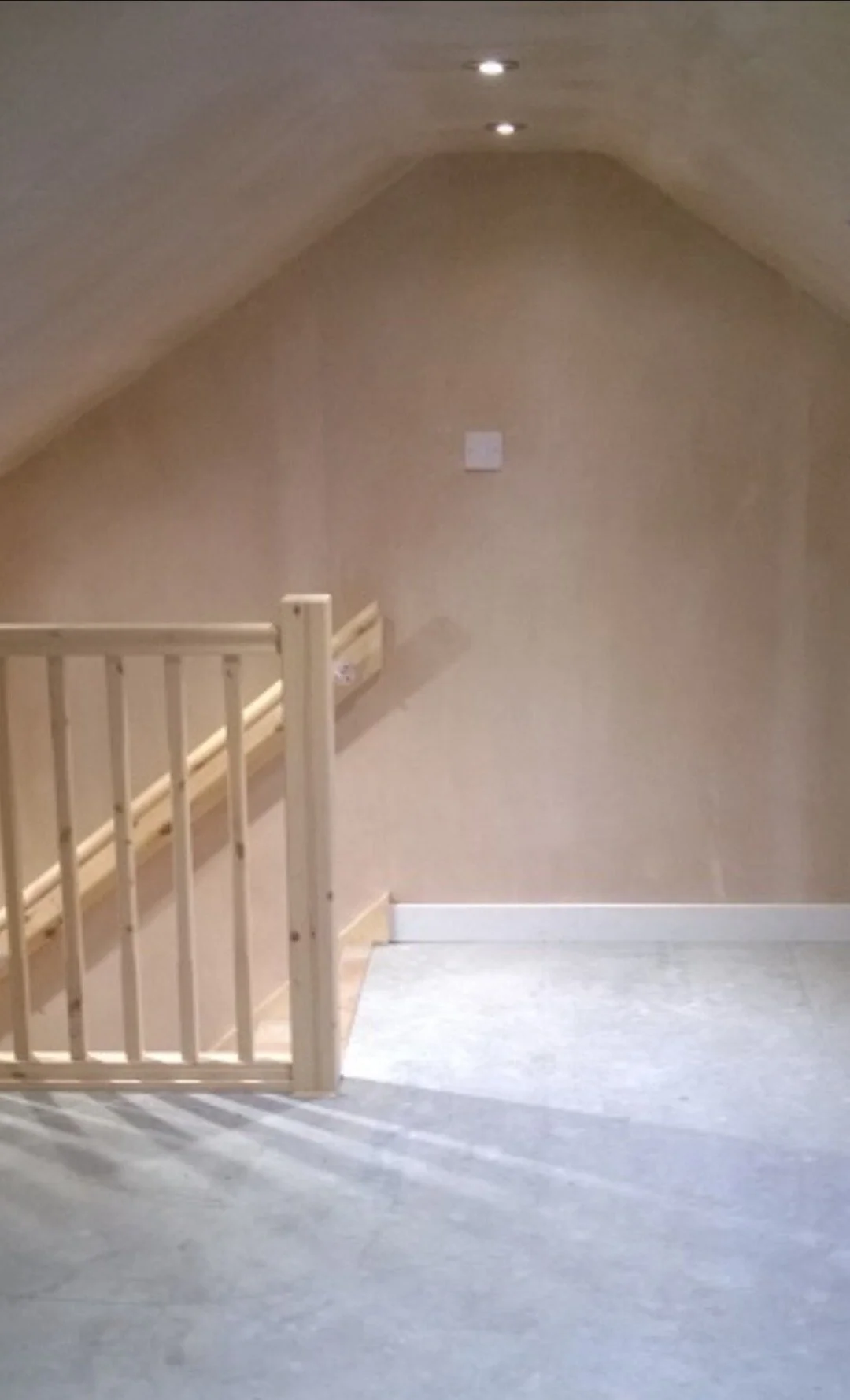 Empty room with beige walls, ceiling with two recessed lights, wooden staircase, and gray carpeted floor.