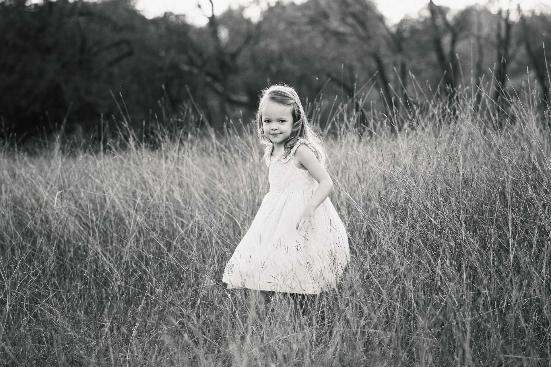 black-and-white-photo-of-a-little-girl-standing-in-a-field-with-tall-grass-near-Southlake-Texas.jpg