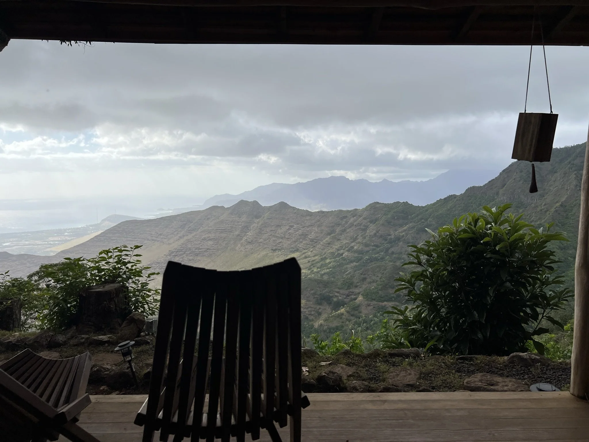 View from a covered porch with two wooden chairs overlooking a mountainous landscape and cloudy sky. Hawaii film, video, photo production service