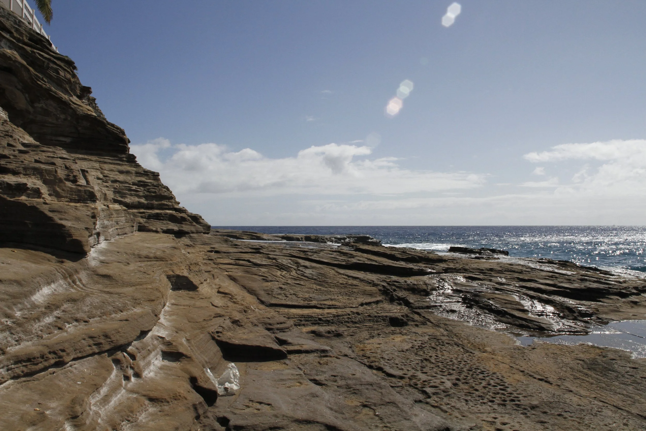 Rocky coastline with layered cliffs and ocean view under a clear blue sky. Hawaii film, video, photo production service