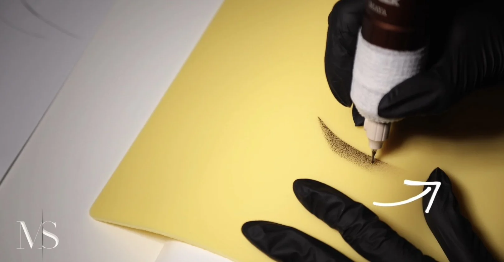 A person wearing black gloves creates a dotted smile on yellow paper with a white marker.