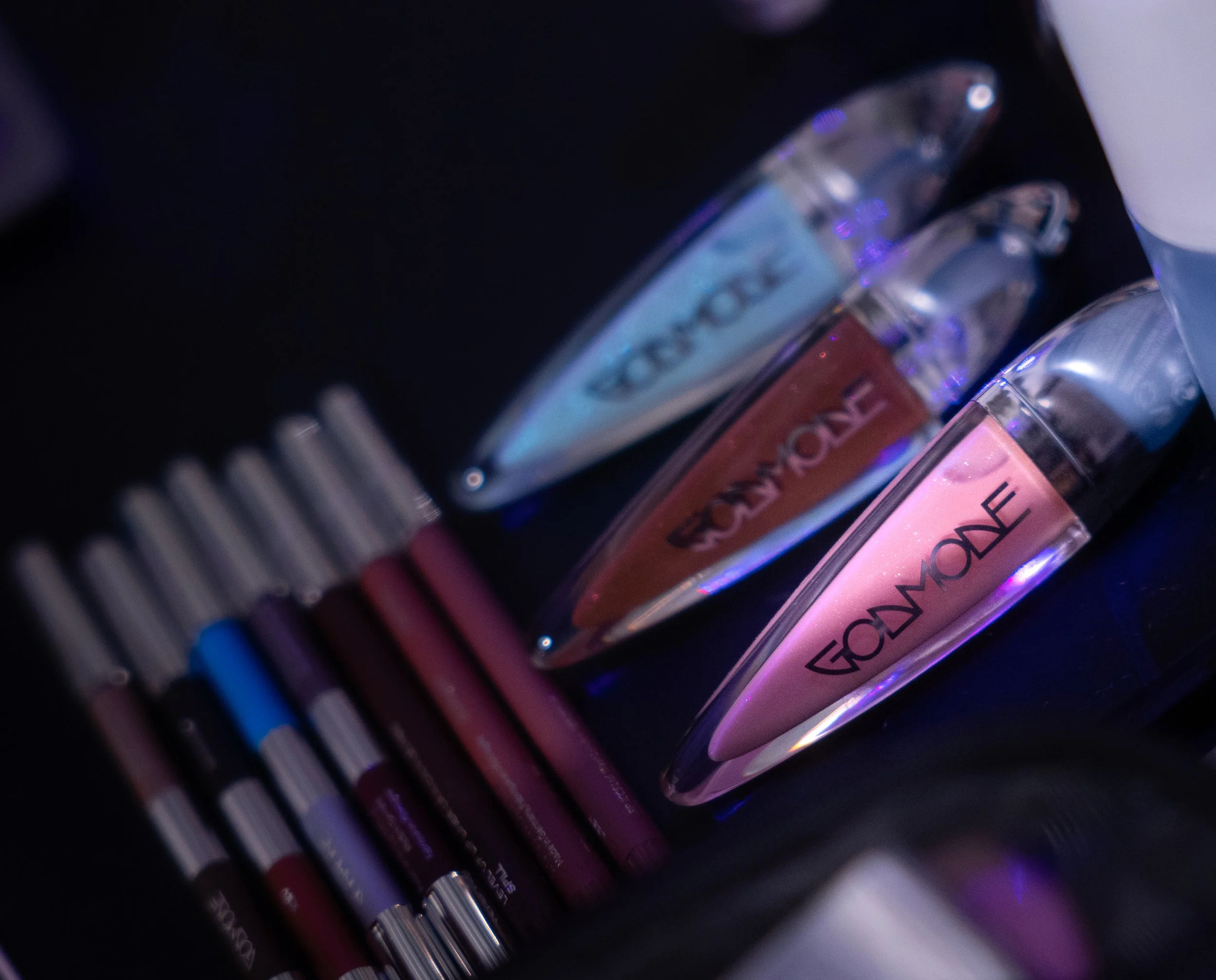 Close-up of three tubes of GLOW ONE skincare products with reflective surfaces, and seven colored markers lined up on a black surface.