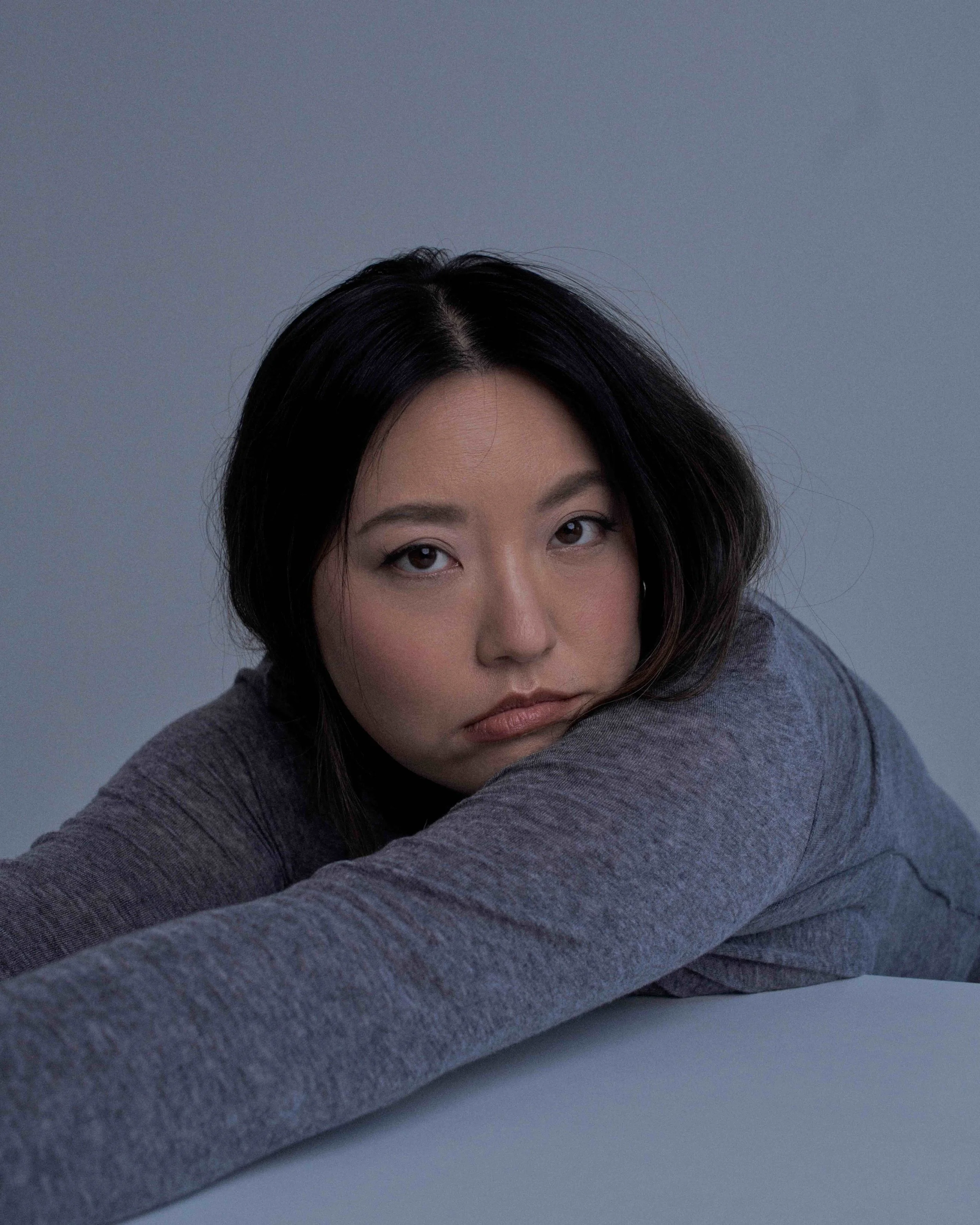 Actress, Jennifer Chung, leaning on a desk with a melancholy look.