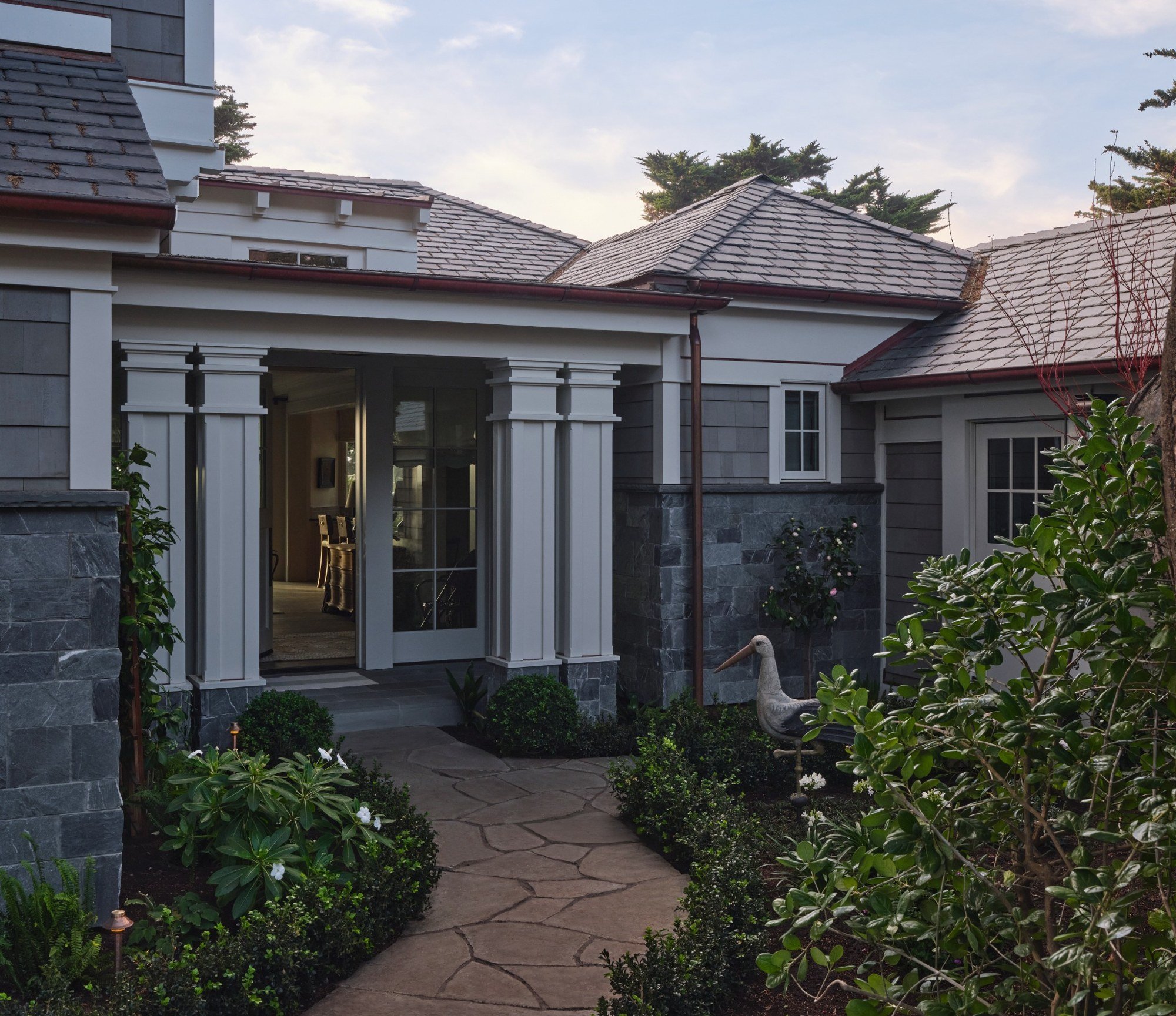 Front view of a house with a stone pathway, garden, and architectural details including columns and gable roofs.
