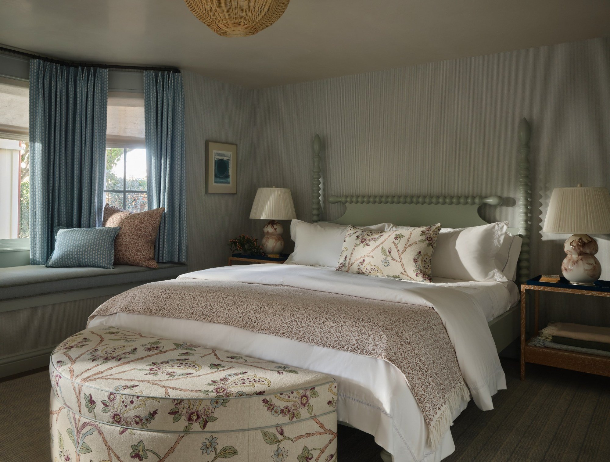 A bedroom with a bed, a window seat with pillows, and blue curtains.
