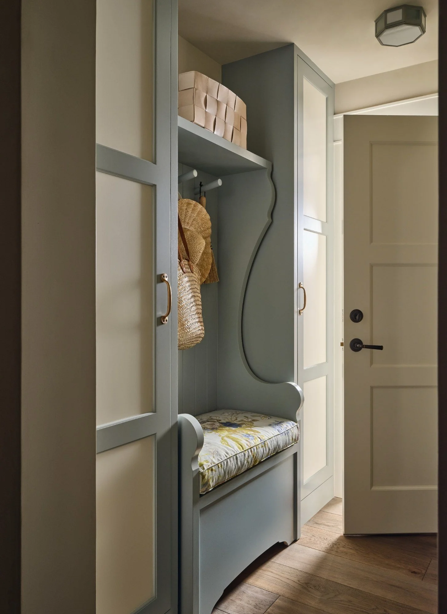 A built-in entryway bench with a cushion, open shelving above with storage baskets, and hooks holding bags, next to a door in a home.