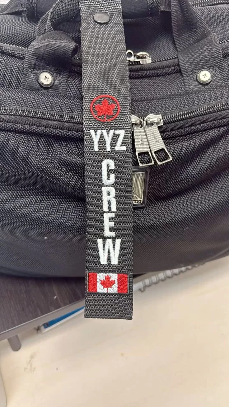 Close-up of a black travel bag with a black strap that has a red and white Canadian flag and the words "YYZ CREW" embroidered on it.