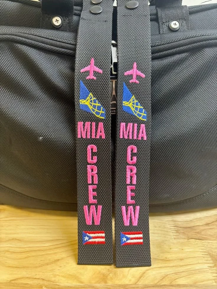 Close-up of black fabric straps with embroidery, including pink airplanes, blue and yellow fish, and Puerto Rican flags, attached to a black backpack.
