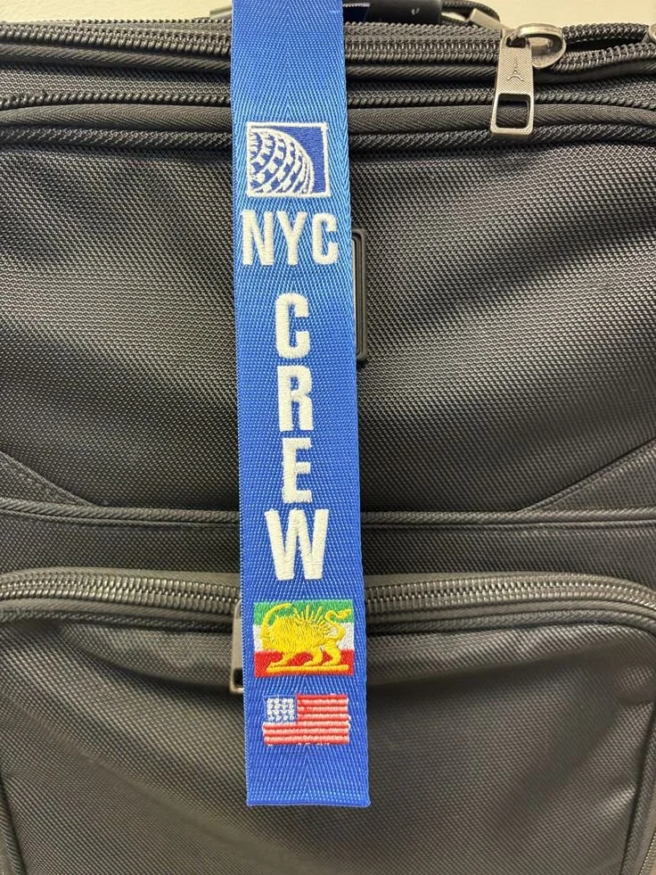 Close-up of a travel backpack with a blue strap that has city and event patches, including NYC, Coney Island with a lion and surfboard, and an American flag.