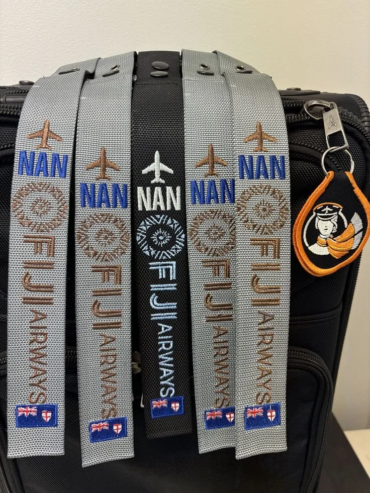 Five embroidered luggage tags hanging on a black suitcase, each with an airplane graphic, the name Nana, and the National Flag of Australia, plus a luggage tag with an astronaut graphic.