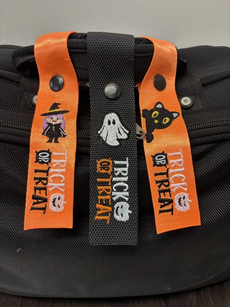 Three Halloween-themed tags on a black bag, featuring a witch, ghost, and black cat, with the text 'Trick or Treat' and small pumpkin icons.