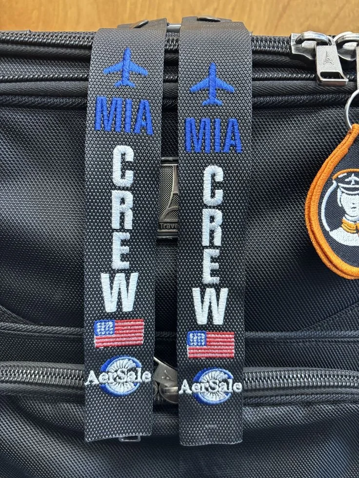 Two luggage tags attached to a black bag, each with a blue airplane icon, the words 'MIA' in blue, 'CREW' in white, a small American flag, and the AeroGle logo.