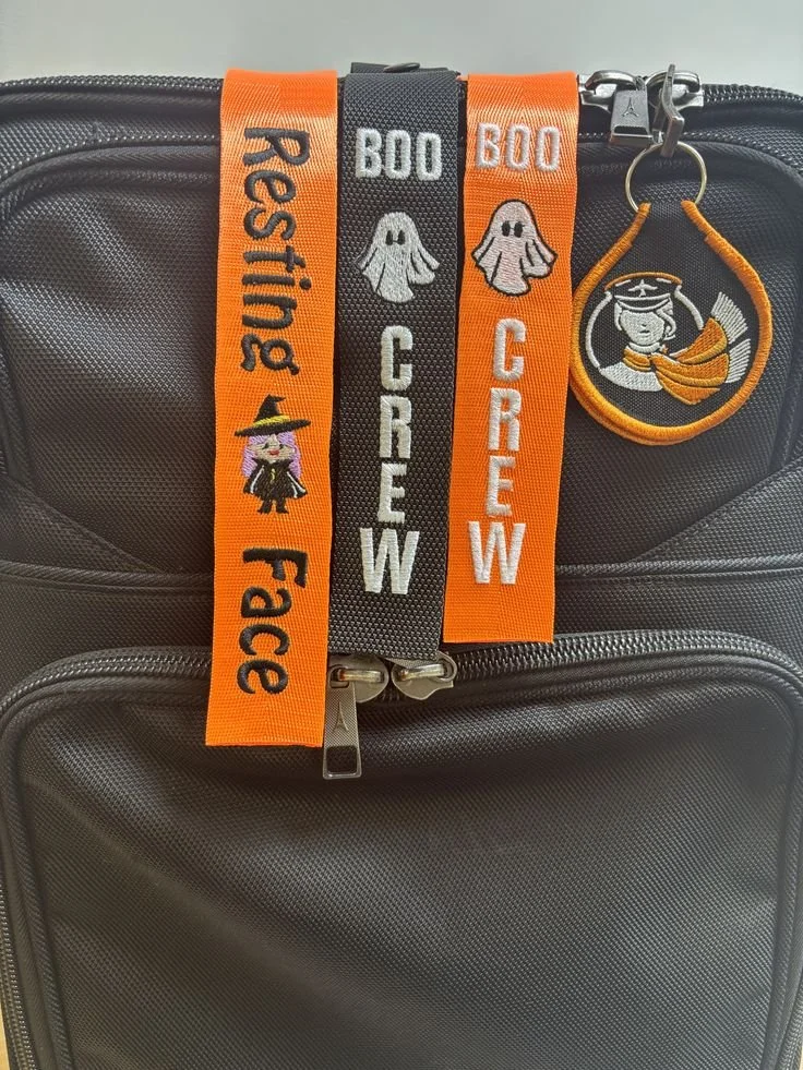 Black suitcase with three Halloween-themed ribbon decorations and a spooky girl keychain.