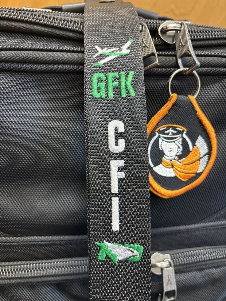 Close-up of a black bag with embroidered patches and keychains, including a patch with a white eagle, green 'GFK' text, and a military emblem with a woman in uniform