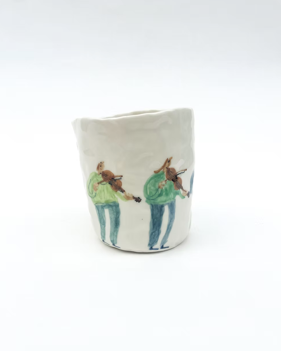 A ceramic cup with hand-painted illustrations of two people playing violins, dressed in green shirts and blue pants.
