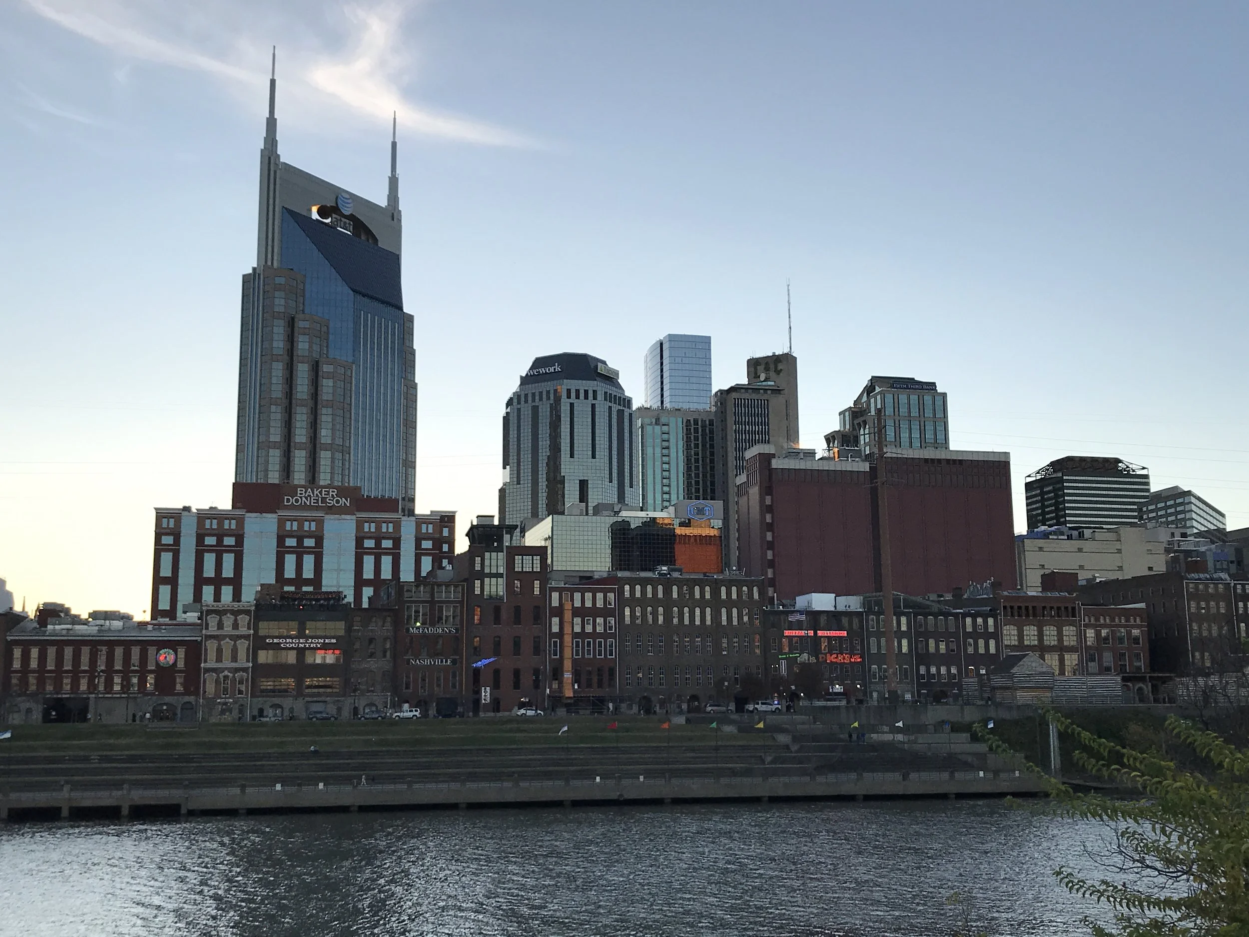 City skyline with tall buildings and a river in the foreground during evening or early night.