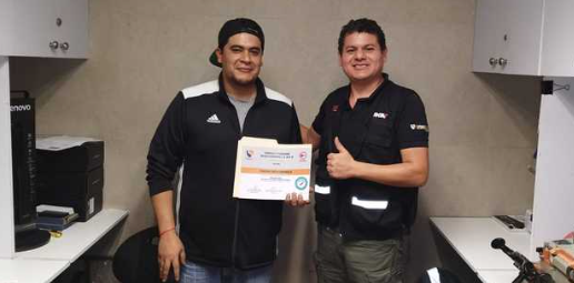 Dos hombres en una oficina, uno sostiene un certificado y ambos sonríen.