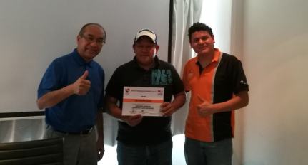 Tres hombres en una sala, uno de ellos sosteniendo un certificado, los otros dos haciendo gestos de aprobación.