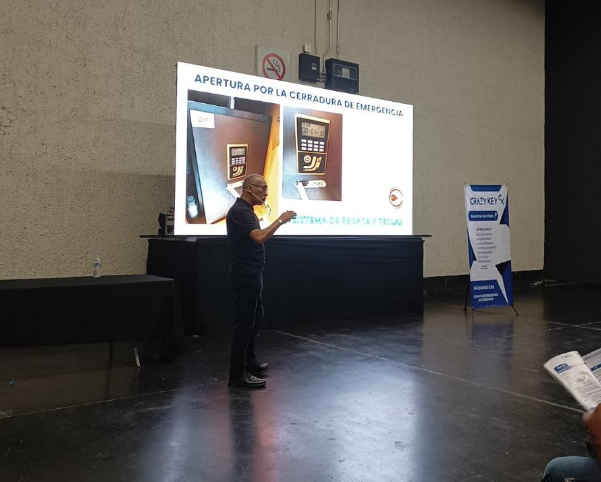 Persona en una sala de conferencias mostrando instrucciones sobre apertura de cerradura de emergencia en una pantalla grande.