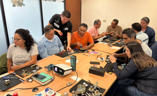 Grupo de personas trabajando en un taller de reparación de relojes en una mesa de madera, con diversas herramientas y relojes en exhibición